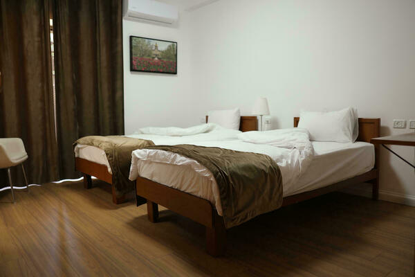 Two single wooden-frame beds with brown blankets and white linens in a room with white walls, wood floors, and brown curtains. A framed picture of the Notre Dame Golden Dome with red tulips hangs on the wall.