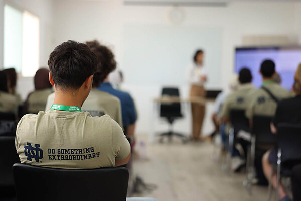 Students listen to a presenter in a classroom, one wears a Notre Dame shirt.