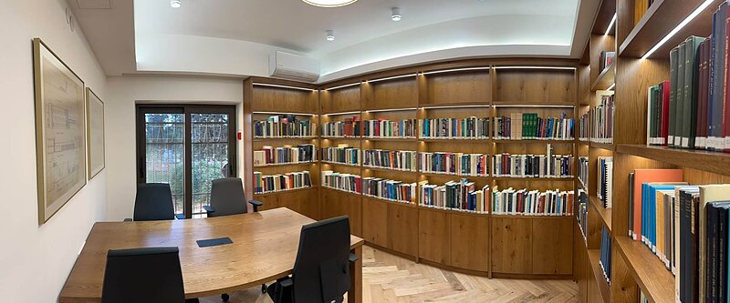 Modern library with a large wooden table, chairs, and floor-to-ceiling bookshelves.